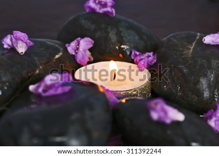 candle on a background of black stones with purple flowers spa salon