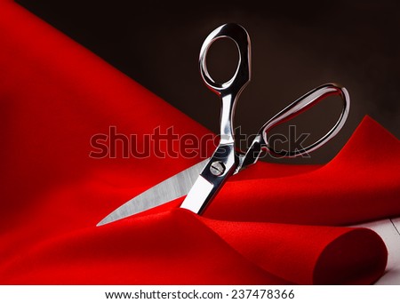 Large tailor scissors cutting a sheet of red fabric