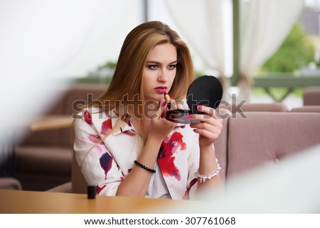girl brushing lips and putting lipstick looking in the mirror at the cafe