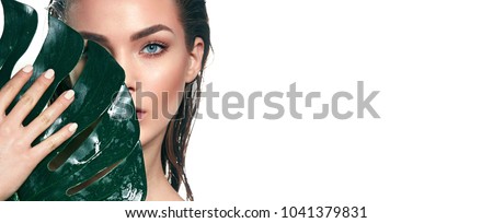 A beautiful young girl in the studio on a white background with wet skin and wet hair holds a large green tropical leaf in hands and covers a part of her face.Fashion, beauty, make-up, cosmetics. Foto stock © 