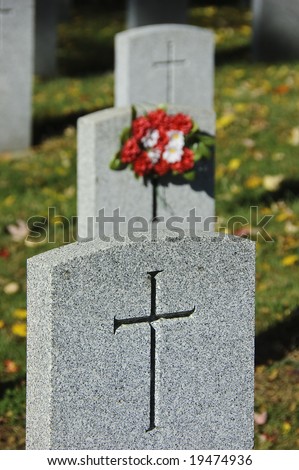 Row of three soldier tombstones marked with crosses and bouquet of red and white flowers on grassy field