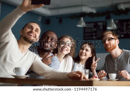 Photo of Excited millennial friends make selfie on smartphone having fun in coffeeshop, happy students smile for picture on phone meeting together in café, diverse young people posing for self-portrait