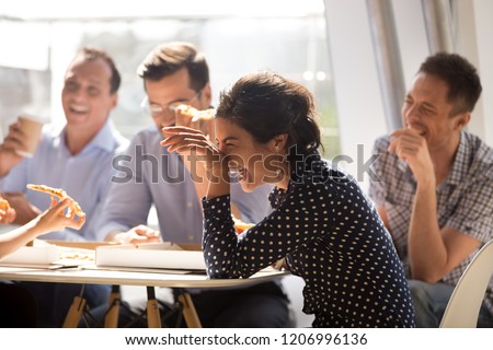 Indian woman laughing at funny joke eating pizza with diverse coworkers in office, friendly work team enjoying positive emotions and lunch together, happy colleagues staff group having fun at break 商業照片 © 