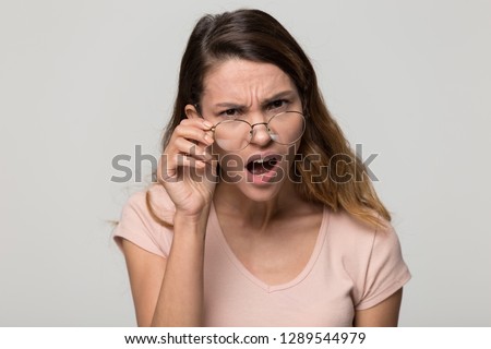 Shocked angry young woman in disbelief lowering glasses looking at camera with indignation isolated on grey blank studio background, confused girl frowning touching eyeglasses feeling flabbergasted Stock foto © 