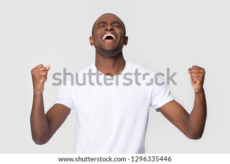 Overjoyed happy young african american man triumphant celebrating lottery betting win screaming with joy isolated on white blank studio background, excited black guy winner rejoicing success victory 商業照片 © 