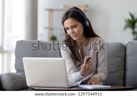 Photo of Happy young woman in headphones speaking looking at laptop making notes, girl student talking by video conference call, female teacher trainer tutoring by webcam, online training, e-coaching concept