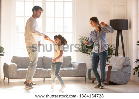 Family mother father and preschool adorable daughter in living room moving dancing to music little girl holding father hand having fun enjoy time with parents at home. Funny leisure activities concept