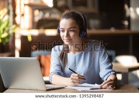 Focused woman wearing headphones using laptop in cafe, writing notes, attractive female student learning language, watching online webinar, listening audio course, e-learning education concept Stock foto © 