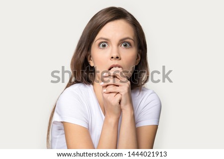 Headshot of frightened woman looking at fear eyes wide open. Studio portrait of terrified, stressed, scared to death young female biting her finger isolated on gray background. People emotions concept Foto d'archivio © 