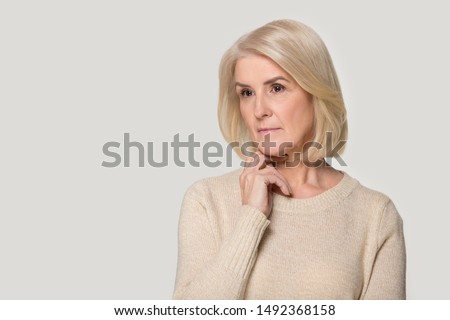 Pensive beautiful senior woman wearing sweater isolated on grey studio background thinking considering idea, thoughtful aged female stand near blank copy space making decision contemplating ストックフォト © 