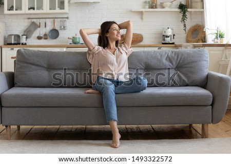 In cozy living room happy woman put hands behind head sitting leaned on couch 30s european female enjoy lazy weekend or vacation, housewife relaxing feels satisfied accomplish chores housework concept 商業照片 © 