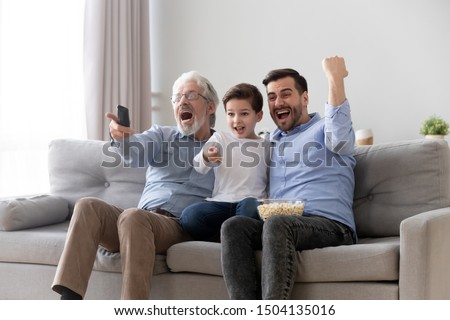 Excited three generation men family fans hold remote control watch tv sport game sit on sofa together, happy grandson young father and old grandfather celebrate goal television team victory at home Photo stock © 