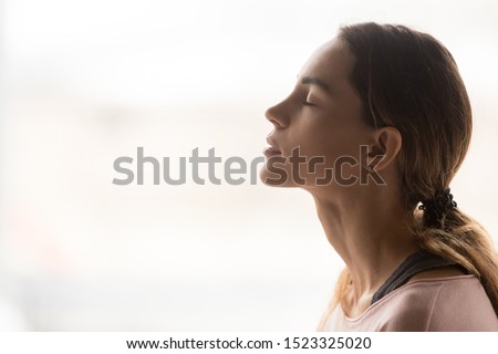 Serene young woman taking deep breath of fresh air relaxing meditating with eyes closed enjoying peace, calm girl tranquil face doing yoga pranayama exercise feel no stress free relief, side view