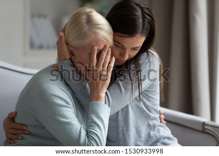  Empathic young lady embracing soothing crying depressed elder mommy, sitting together at home. Upset loving grown up millennial daughter cuddling supporting depressed stressed middle aged mother. Stockfoto © 