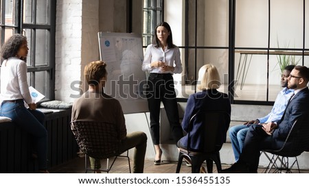 Confident lady business trainer coach leader give flip chart presentation consulting clients teaching employees training team people speaking explaining strategy at marketing workshop concept