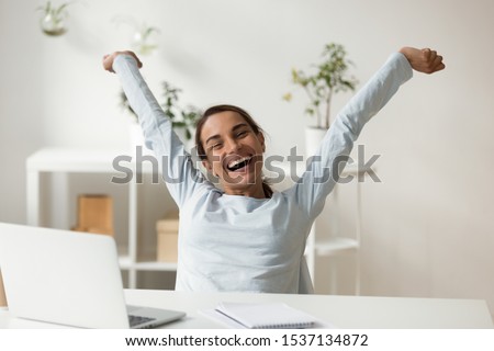 Head shot portrait overjoyed smiling young mixed race lady rising hands, stretching back, relaxing after finishing project. Happy millennial woman employee celebrating working day finish at office. 商業照片 © 