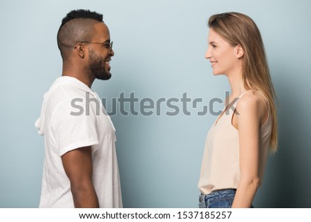 Smiling multiracial millennial man and woman isolated on blue studio background stand in profile look at each other, side view of happy multiethnic couple posing laughing, international love concept ストックフォト © 