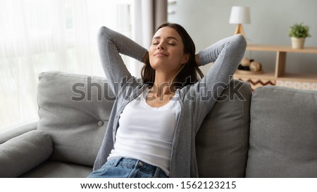 Relaxed serene pretty young woman feel fatigue lounge on comfortable sofa hands behind head rest at home, happy calm lady dream enjoy wellbeing breathing fresh air in cozy home modern living room Foto stock © 