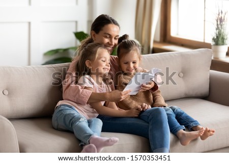 Happy family young mother babysitter hold read book relax embrace cute little children daughters, smiling parent mum tell small kids funny fairy tale story sit on sofa having fun together at home Foto stock © 