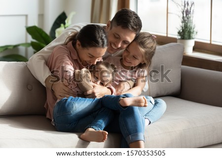 Happy cheerful parents having fun with cute children daughters cuddling playing on sofa together, mom and dad laughing embracing little kids daughters tickling enjoying family lifestyle games at home