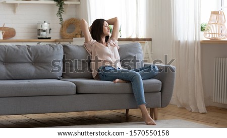 Serene lady housewife lounge sit on sofa feel fatigue napping hold hands behind head, calm young woman rest on comfort couch with eyes closed breath fresh air in cozy clean modern living room at home