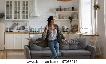 Carefree happy single young attractive woman dancing alone in modern kitchen interior, independent active lady having fun at clean home listening music enjoying freedom weekend time lifestyle at home