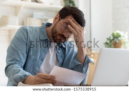 Upset frustrated young man reading bad news in postal mail letter paper document sit at home table, depressed stressed guy worried about high bill tax invoice, overdue debt notification money problem Foto stock © 