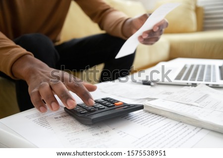 Close up of african American man calculating using machine managing household finances at home, focused biracial male make calculations on calculator paying bills, account taxes or expenses