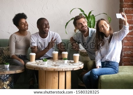 Photo of Smiling multiracial millennial friends have fun in coffeeshop drink coffee making self-portrait picture together, happy diverse multiethnic young people pose for selfie chill hang out in café