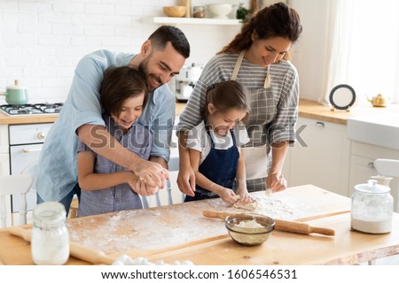 Full family feels happy cooking together gathered in domestic kitchen preparing family recipe pie or dessert, playful siblings helping to parents, mom and dad teaching kids, hobby and pastime concept