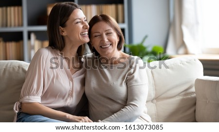 Happy senior mother and grownup daughter sit relax on couch in living room talk laugh and joke, smiling overjoyed middle-aged mom and adult girl child rest at home have fun enjoying weekend together