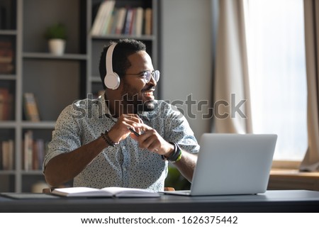 Happy relaxed millennial afro american business man wear wireless headphones look away rest at workplace finished work listening music podcast feel peace of mind concept sit at desk in sunny office