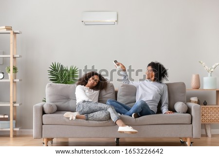 Happy african family relax on sofa under air conditioner, black mom holding remote control switch on conditioning in living room adjust comfort temperature for daughter, climate system at modern home