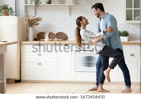 Happy loving young couple dancing romantic dance on date in modern kitchen, smiling husband and wife celebrating anniversary, enjoying tender moment, having fun, moving to music at home
