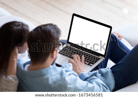Loving couple looking at laptop screen blank white mockup close up, sitting on cozy sofa, young man and woman reading email, message, searching information in internet, shopping or chatting online
