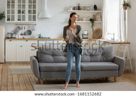 Overjoyed young woman enjoy free leisure weekend at home dancing listen to music in living room, smiling happy millennial female have fun moving to rhythm being active in modern studio home