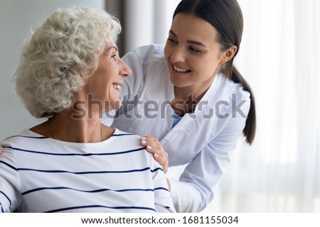 Caring young nurse support assist positive old lady patient at home or hospital, smiling female caregiver or doctor give help to optimistic mature senior grandmother, elderly healthcare concept