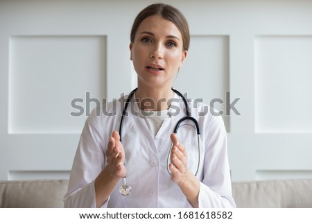 Head shot portrait woman doctor talking online with patient, making video call, looking at camera, young female wearing white uniform with stethoscope speaking, consulting and therapy concept