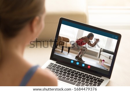 Focus on laptop screen with young woman in sportswear doing morning exercises, deep squats on yoga mat, staying fit at home. Interested girl watching online educational fitness workshop training.