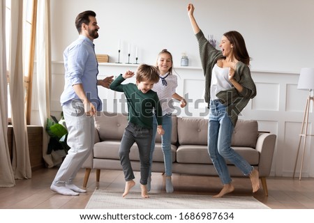 Full length overjoyed married couple dancing to favorite music in living room with adorable two children siblings. Excited happy kids son daughter having fun with energetic young parents at home.