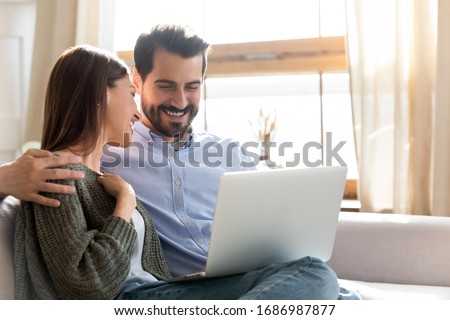 Head shot smiling young woman watching comedian movie or funny videos on computer with loving husband at home. Happy married couple spending free leisure weekend holiday time with laptop indoors.