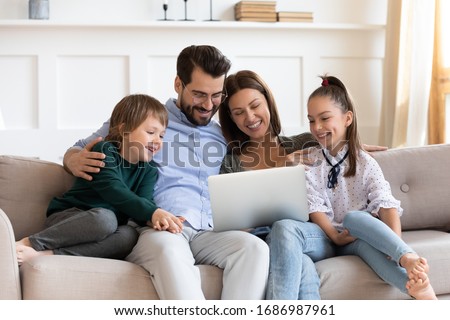 Smiling parents cuddling little kids, looking at laptop screen. Happy family couple watching funny movies or cartoons, having fun together in living room, relaxing on sofa, enjoying weekend time.