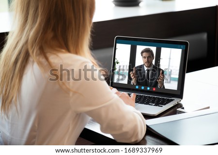 Back view of female employee talk on video call with male colleague or business partner, woman worker communicate online speak on Webcam, have web conference with coworker from home office