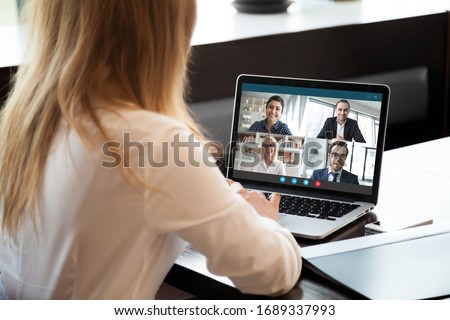 Back view of businesswoman speak using Webcam conference on laptop with diverse colleagues, female employee talk on video call with multiracial coworkers engaged in online briefing from home