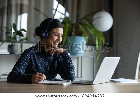 Happy young indian girl with wireless headphones looking at laptop screen, reading listening online courses, studying remotely from home due to pandemic corona virus world outbreak, quarantine time. Stock foto © 