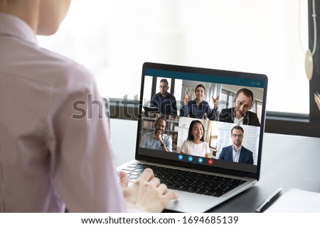 Computer monitor view over female shoulder during group video call with multi-ethnic international colleagues or friends. Distant communication and working use on-line app, internet connection concept