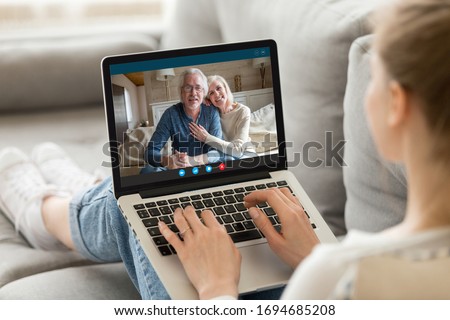 Over girl shoulder pc screen view, sit on sofa living in country grandparents communicating with adult granddaughter via videocall. Parents and grownup daughter talking use videoconference app concept