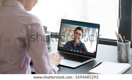 Indian girl communicate with friend on-line by video call, pc screen view over female shoulder. Mental health expert online therapy, colleagues work on common project use videoconferencing app concept Foto d'archivio © 
