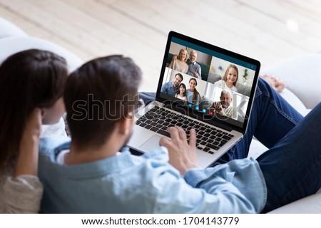 Rear back view married couple resting and chatting with relatives via videoconference videocall application, laptop screen view over spouse shoulder. Distant virtual communication, modern tech concept