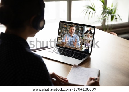 E-learning via virtual application, videocall video conferencing activity, colleagues working together concept. Pc screen view over woman shoulder, listen tutor gain new knowledge noting information